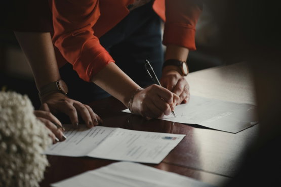 person-in-orange-long-sleeve-shirt-writing-on-white-paper.jpg person in orange long sleeve shirt writing on white paper